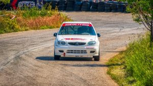 A rally car speeds through a curvy track surrounded by greenery in Ritsona, Greece.